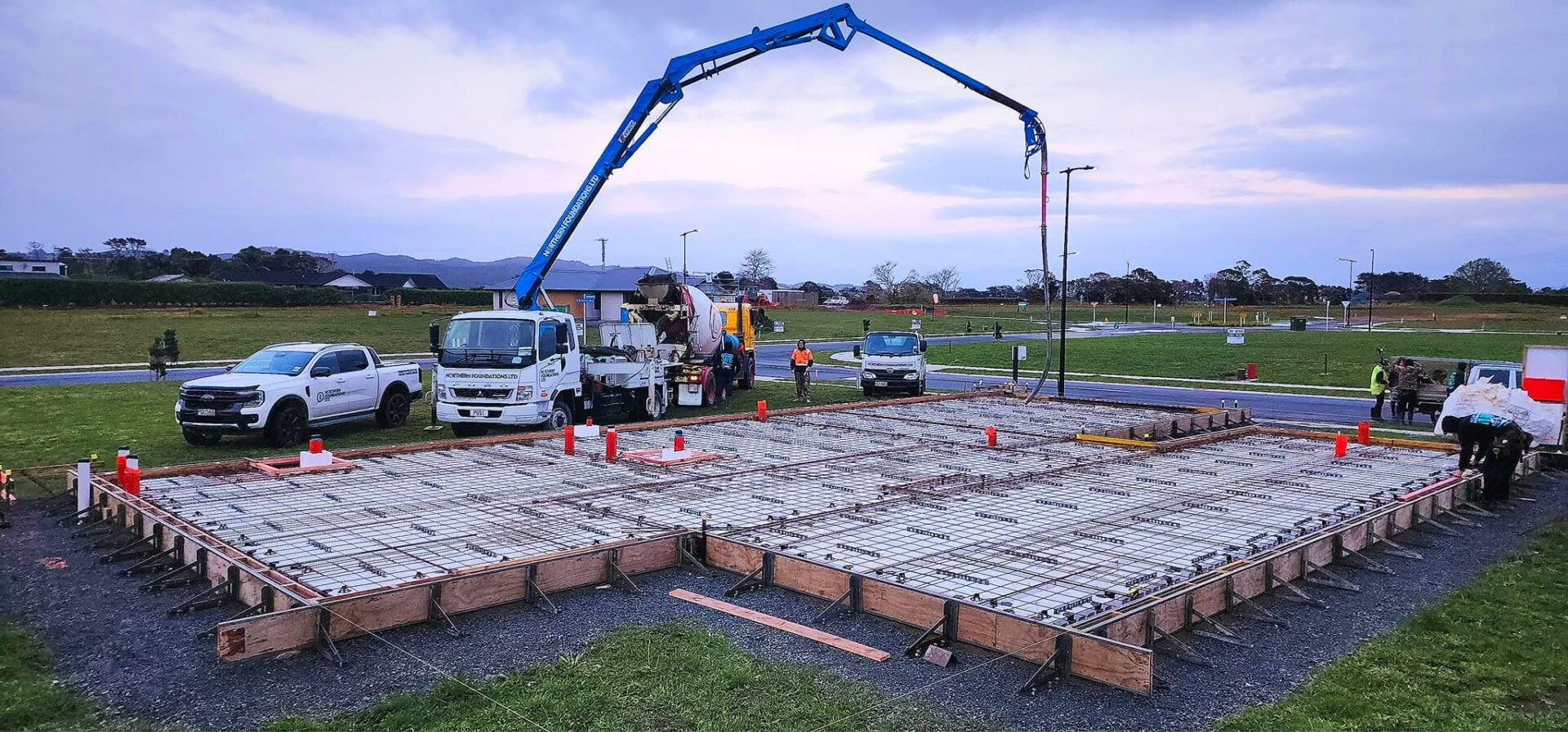 The boom pump reaching over a rib raft foundation, with utes and a concrete truck on site