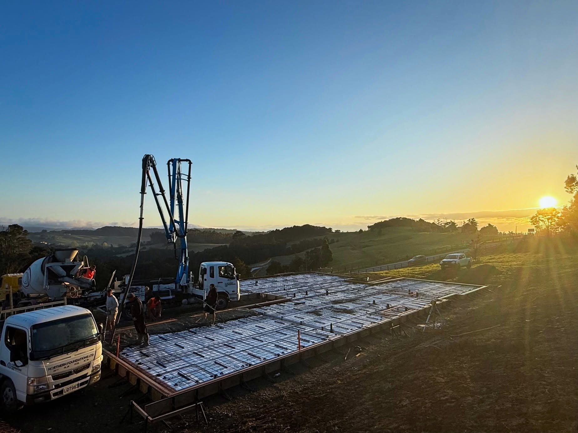 A Northern Foundations boom pump and crew placing concrete on a foundation at sunset